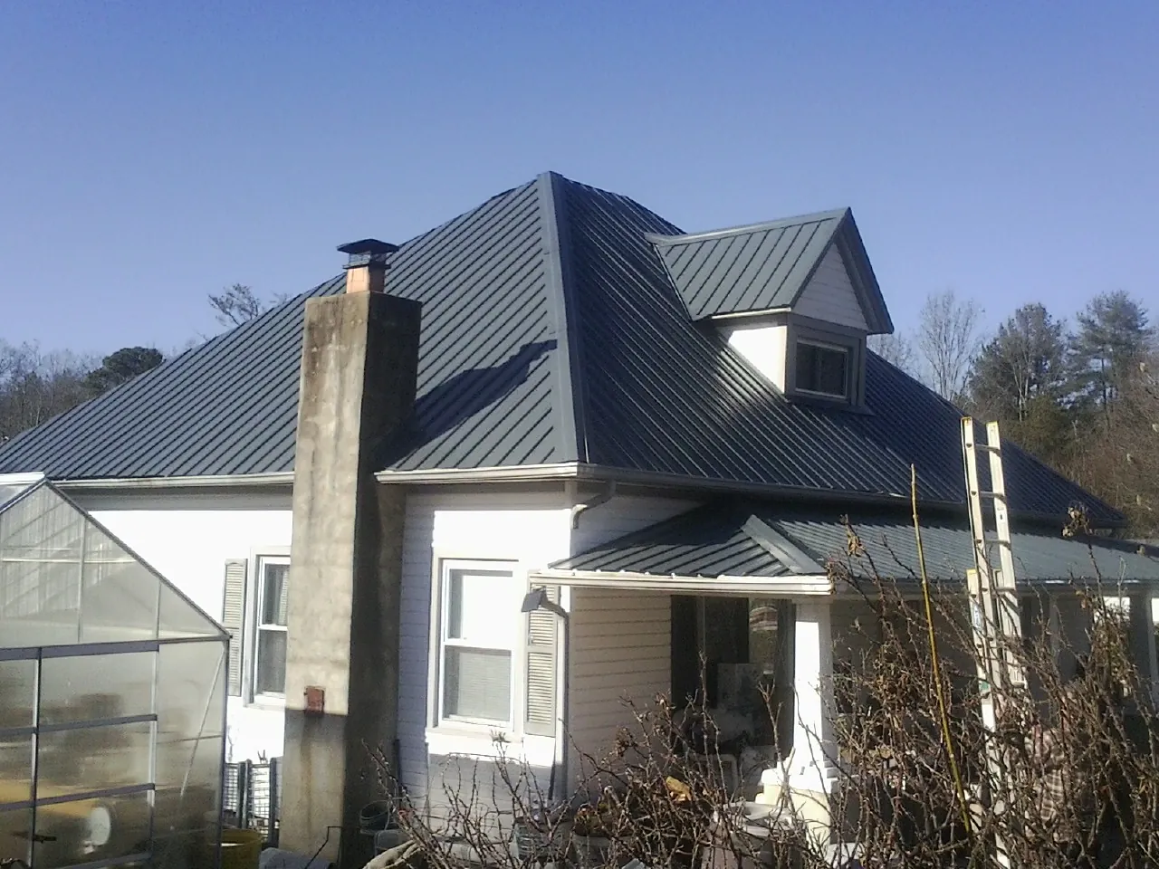 Dark blue standing seam metal roof on a white farmhouse with dormer — Slate & Tile Roof Repair by Roofing Brothers in Chardon
