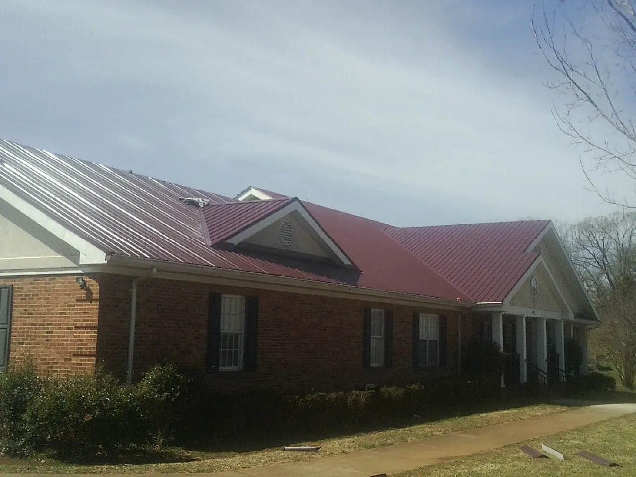 Red metal roof with gabled entries on a long brick building, from a Hail Damage Roof Repair job in Chardon