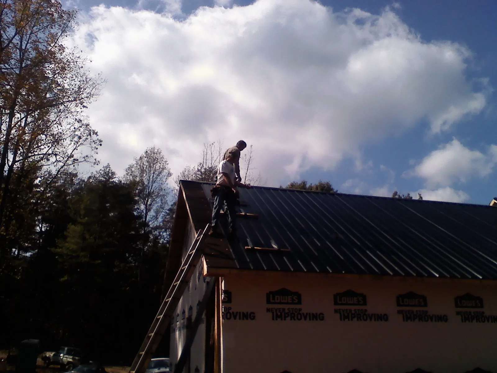 Roofer fastening dark metal panels high against a cloudy sky, from a Roof Inspection job in Chardon