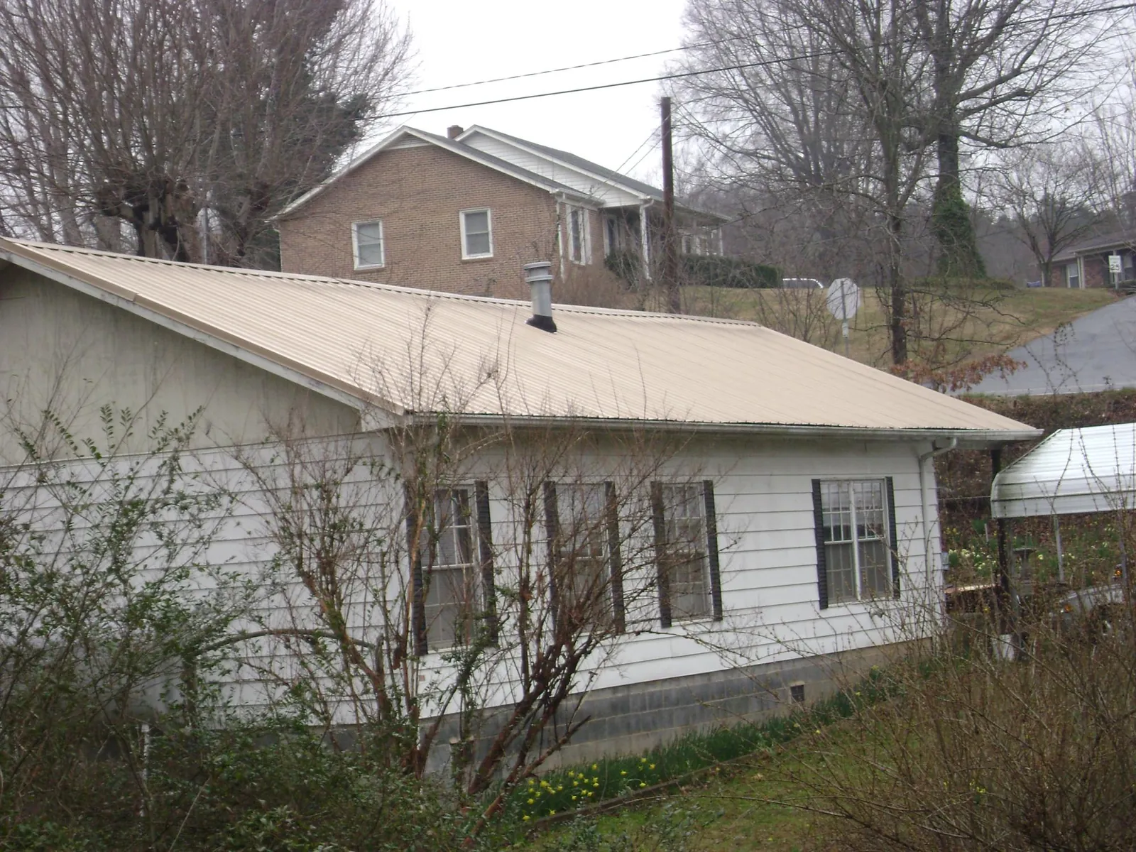 Tan metal roof on a white sided house set into a hillside — Commercial Roofing by Roofing Brothers in Chardon