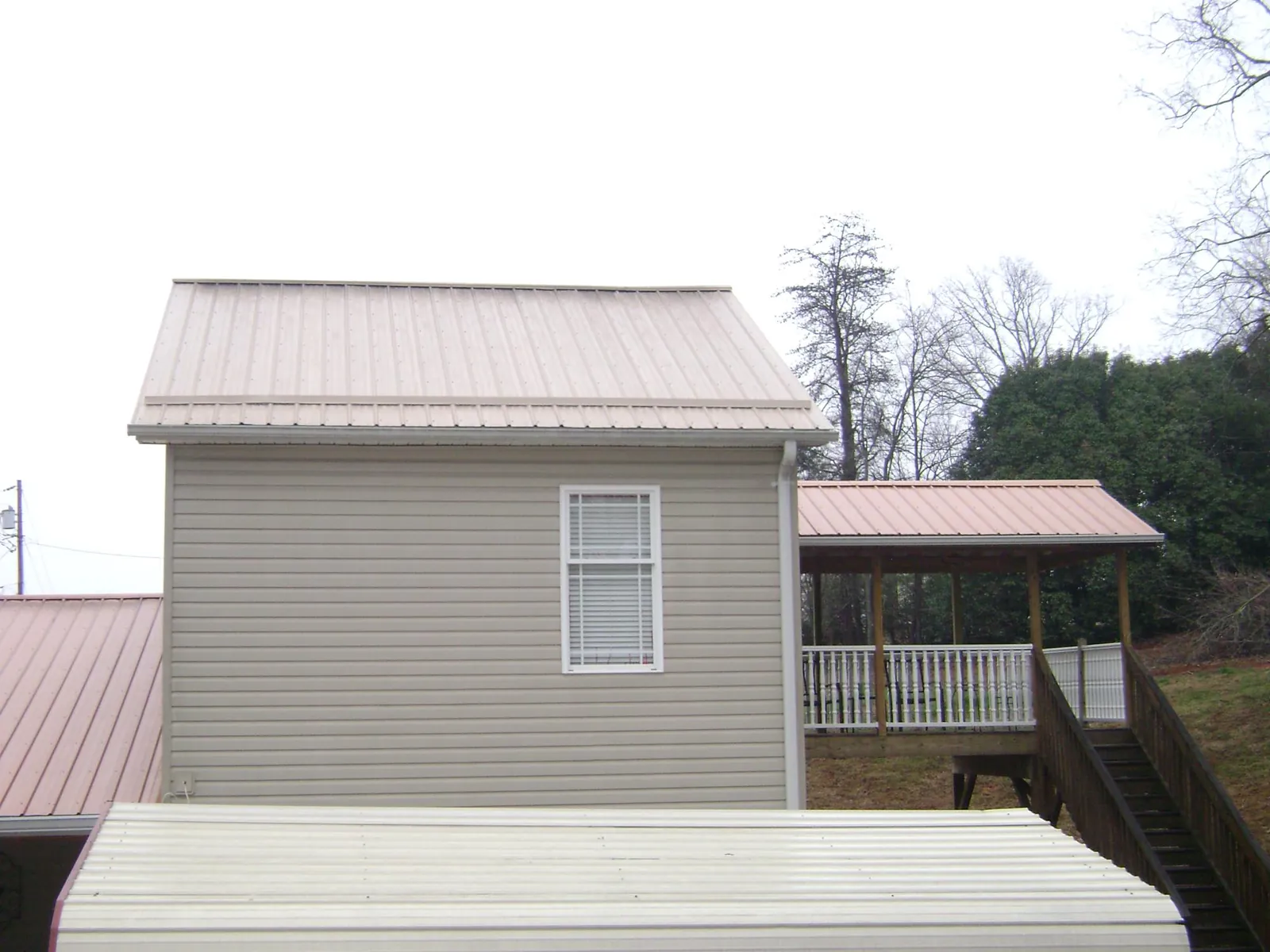 Tan metal roofs on a two story addition and attached porch, from a Roof Replacement job in Chardon